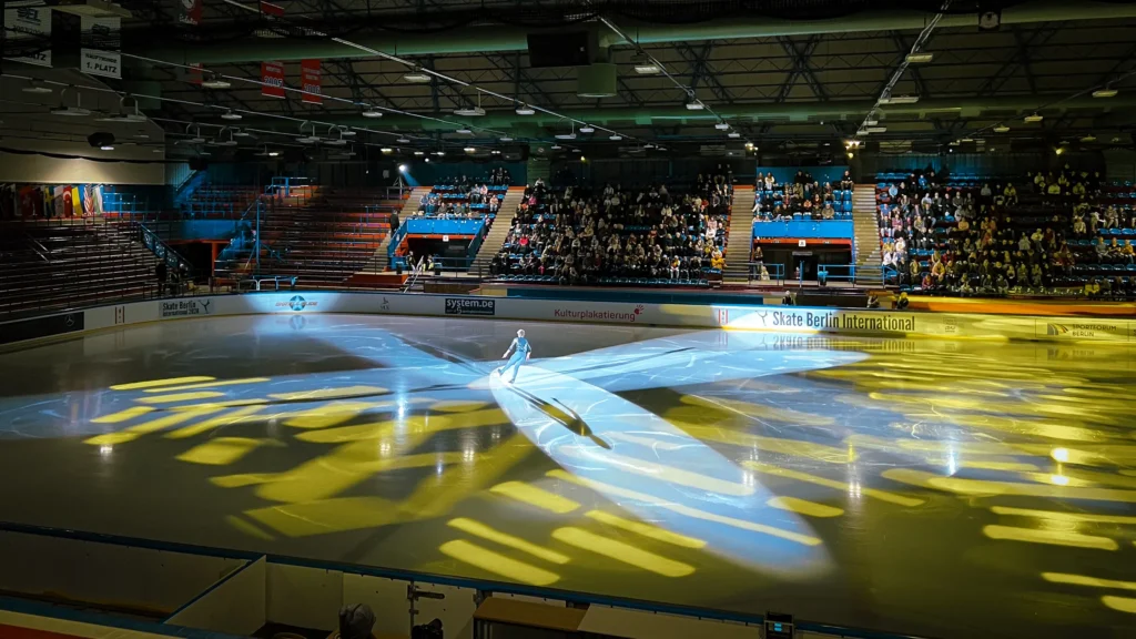 Photo: Florian Knorn Light show at the SBI26 exhibition in the “Wellblechpalast”: a spotlight and yellow patterns on the ice, well-filled stands behind.